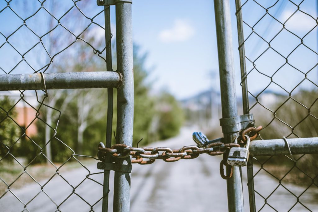 La imagen muestra una cadena oxidada con candados que sujetan las puertas de alambre de la cerca.